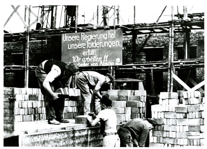 Nach der blutigen Niederschlagung des Volksaufstands nehmen die Bauarbeiter die Arbeit wieder auf. Im Hintergrund ein Propaganda-Plakat, das vom Versagen der SED-Führung ablenken soll. Quelle: DHM
