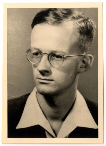 Das Schwarz-Weiß-Porträtfoto zeigt einen jungen Mann. Er trägt eine runde Brille mit Drahtgestell, eine dunkle Jacke und ein helles Hemd mit Kragen.