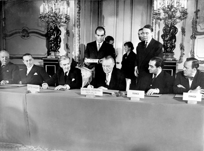 Großbritanniens Außenminister Antony Eden, Bundeskanzler Konrad Adenauer und Frankreichs Ministerpräsident Pierre Mends-France (ab dem 3. v. l.) unterzeichnen die Schlussakte der Londoner Neunmächtekonferenz im Oktober 1954. Hierin erklären sie ihre...