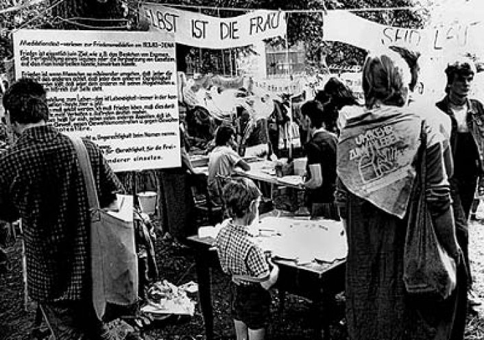 Während der Friedenswerkstätten in der Berliner Erlöserkirche verbreiten oppositionelle Gruppen Infoblätter zu verschiedenen Themen. Am Stand der Frauen für den Frieden am 3. Juli 1983 verteilen Bärbel Bohley und Gisela Metz Informationen zur Wehrdienstverweigerung.