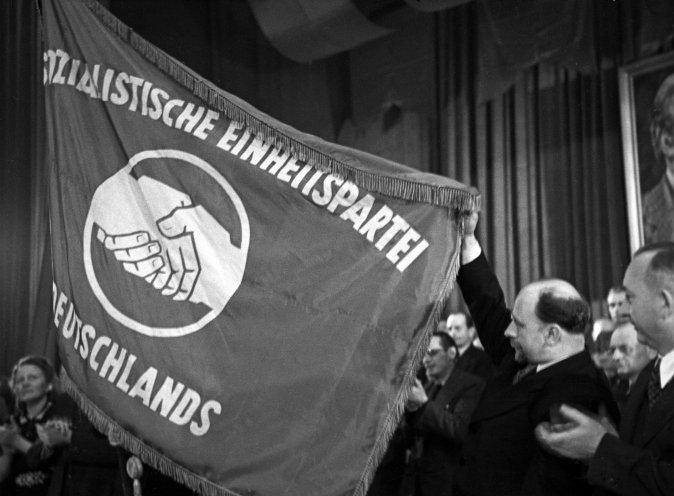 Walter Ulbricht (2. v. r.) präsentiert im Admiralspalast die neue Fahne der SED mit dem Symbol des historischen Händedrucks zwischen Kommunisten und Sozialdemokraten. In der Bevölkerung der SBZ hat die „Russenpartei“ jedoch zunächst wenig Rückhalt....
