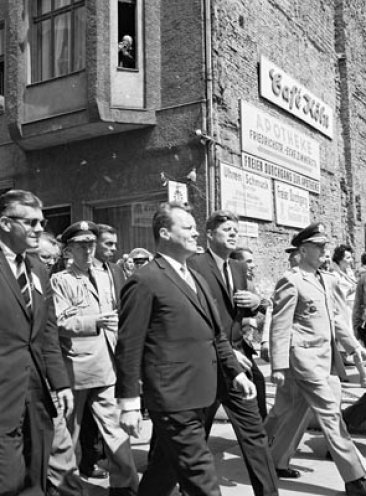 Präsident John F. Kennedy (Mitte) und links neben ihm Willy Brandt, der Regierende Bürgermeister von West-Berlin, auf dem Weg zum Ausländerübergang Checkpoint Charlie.