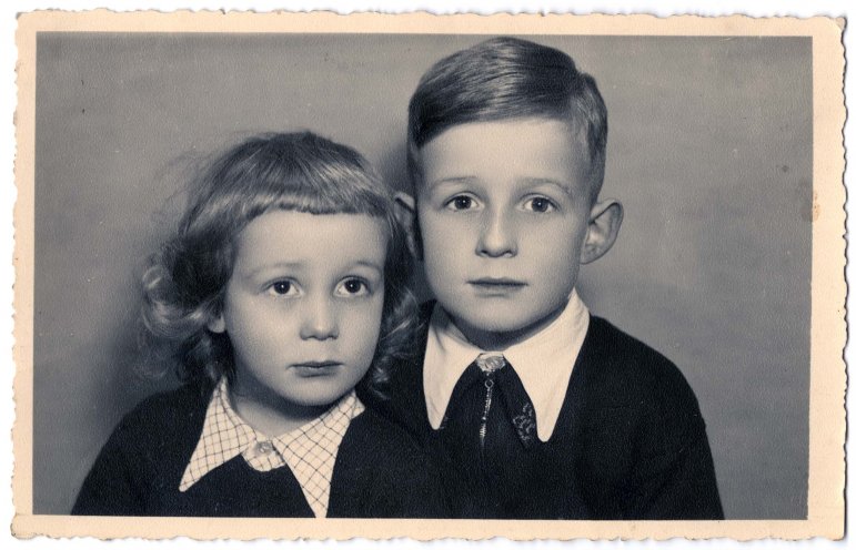 Auf dem Schwarz-Weiß-Porträtfoto sieht man zwei kleine Kinder. Die beiden Kinder tragen ähnliche Kleidung - dunkle Pullover und weiße Hemden mit Kragen. Der Junge auf der linken Seite hat lockiges Haar und der Junge auf der rechten Seite ordentlich gekämmtes Haar.