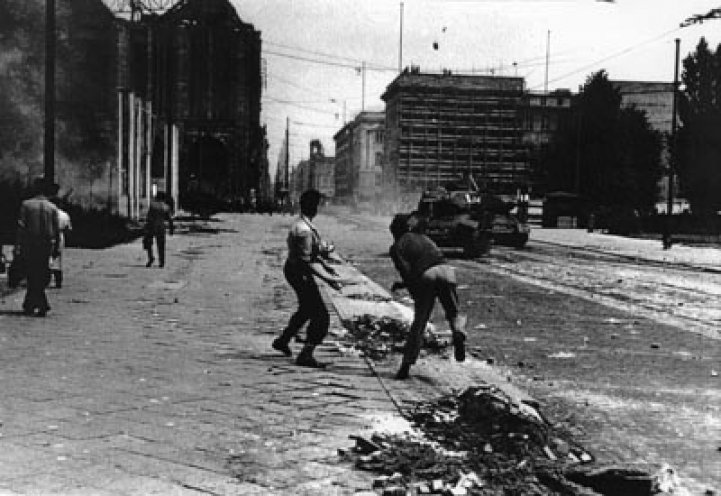 Ein ungleiches Duell: Die Jugendlichen Hans Joachim Maitre (l.) und Erwin Kalisch (r.) gehen in der Leipziger Straße mit Steinen gegen sowjetische Panzer vor. Der 19-jährige Hans Joachim Maitre wird nach dem Aufstand verhaftet und wegen „Anstiftung...
