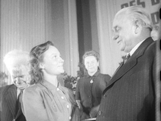 Das jüngste Mitglied der Provisorischen Volkskammer, Margot Feist, die spätere zweite Ehefrau von Erich Honecker, gratuliert Wilhelm Pieck zu seiner Wahl zum ersten Staatspräsidenten der DDR. Links im Bild Hermann Matern, Mitglied des Parteivorstandes...